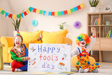 Funny little children in clown costumes with poster at home. April Fools' Day celebration
