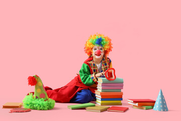 Funny little girl in clown costume with megaphone and books on pink background. April Fools' Day celebration