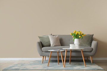 Stylish interior with grey sofa and vase of yellow tulips on coffee table