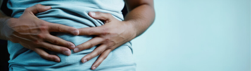 Banner closeup of man holding his stomach with both hands on light background with space for text. Suffering from abdominal pain, expectation or anxiety, acute pain, analgesics - obrazy, fototapety, plakaty