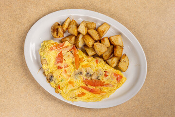 A mushroom and red pepper omlette with hash broown potatoes on a white plate