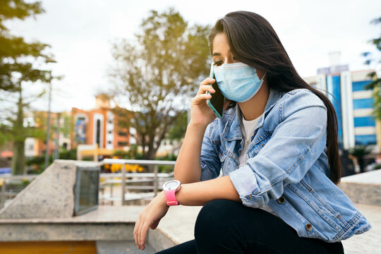 Beautiful woman with mask sitting in the park calling with cell phone