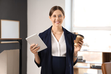 Young pregnant businesswoman with tablet computer and coffee cup in office