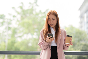 Businesswoman holds a phone and a cup of coffee while walking on the walkway to her office. overview of the lifestyle of business women