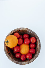 red and yellow tomatoes covered with water drops in a wooden bowl on a white background