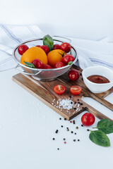 red cherry tomatoes on branches and yellow tomatoes in a colander with basil leaves, on a wooden...