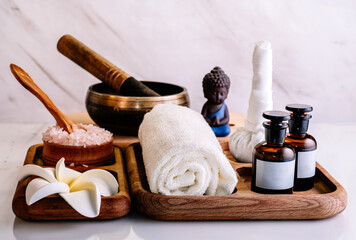Spa composition with Buddha, singing bowl, herb massage bag, sea salt and aroma oil on wooden tray on marble wall background.