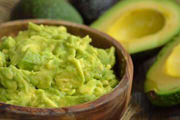 Obraz premium Close-up of homemade guacamole in a wooden bowl with ripe avocados beside it, ideal for culinary themes.