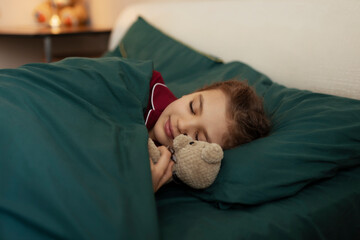 7 year old girl in red pyjamas sleeps in green bed with her teddy bear toy at home