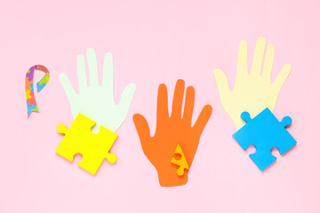 Paper hands, puzzle and awareness ribbon on pink background. Concept of autistic disorder