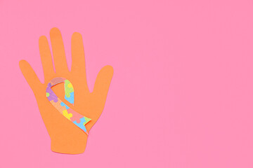 Paper hand and awareness ribbon on pink background. Concept of autistic disorder