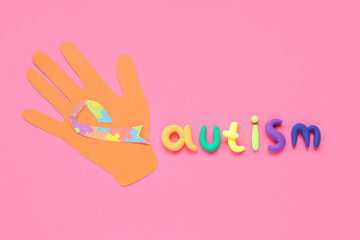 Paper hand and word AUTISM on pink background. Concept of autistic disorder