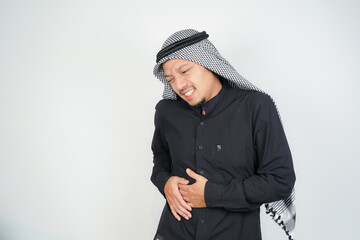 Muslim man wearing Arab turban sorban having stomach ache, bending over, holding hands on stomach,...