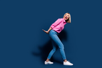 Full size photo of good mood girl dressed pink shirt jeans pull imaginary box look empty space isolated on dark blue color background