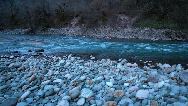 Mountain river bank along which a blue river flows near the shore stones
