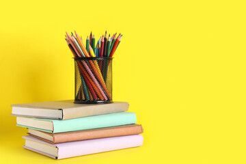 Fototapeta premium Pencil holder full of colorful pencils and books on yellow background. End of school