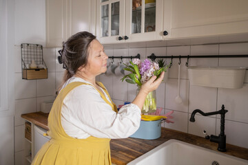 happy mature woman with beautiful bouquet of hyacinths in kitchen, spring home cleaning, highlighting satisfaction in freshness and beauty spring
