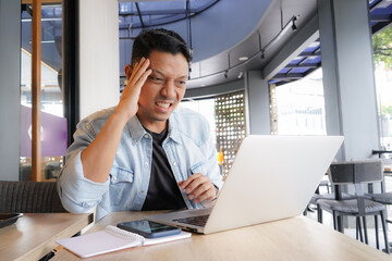 Fototapeta premium Asian man get pressure Tired headache, having Neck Pain, using laptop, mobile phone in coffee shop, online business
