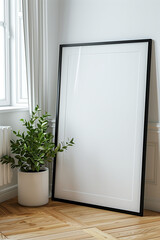 A white poster frame mockup is leaning against the wall. It has a black thin frame with wooden edges and is leaning on a parquet floor in a modern interior. Next to it is a green plant in a white pot.