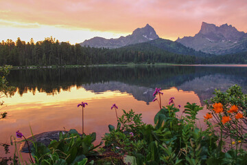 Golden sunset in mountain lake. Two peaks reflected in water. Summer scenery landscape, orange and pink flowers on blank. Travel, touristic destination place. Power of Siberia, Ergaki national park