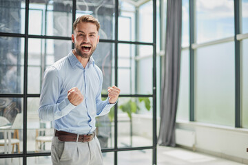 Fototapeta premium Portrait of a young businessman in a blue shirt shaking his fists celebrating his success
