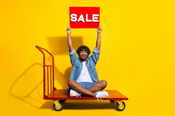 Full body photo of young man ride sit warehouse cart sale plate wear trendy denim clothes red scarf isolated on yellow color background