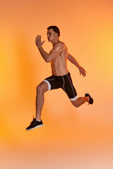 Fototapeta na wymiar attractive shirtless man in black shorts exercising actively and looking away on orange backdrop