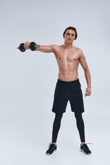 attractive athletic man posing topless exercising actively with dumbbell and looking at camera