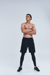 good looking sexy shirtless man in black sporty pants posing on gray backdrop and looking away