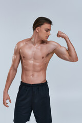 Fototapeta na wymiar sexy shirtless athletic man in black pants playing his muscles while posing on gray background