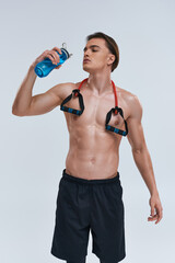 tempting shirtless sporty man in black pants drinking water with fitness expander on his neck