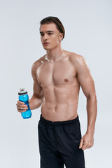 Fototapeta premium handsome sexy male model in black pants holding water bottle and looking away on gray backdrop
