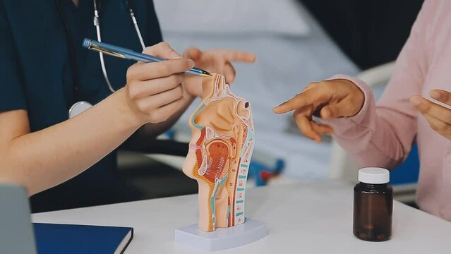 asian female doctor wearing face mask is showing a rectal model and explaining to elder senior man patient in hospital.