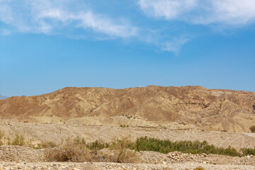Large salt formation mountains, blue sky, sparse clouds. Arid terrain, no visible vegetation. Brown, eroded mountains. Sandstone, pebbles in foreground. Dead sea, Israel. Mountains Sodom and Gomorrah
