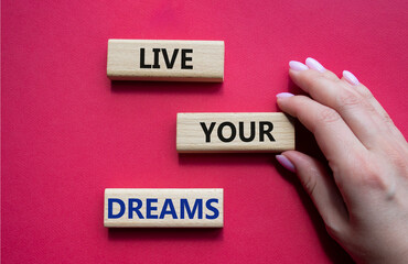 Live your Dreams symbol. Wooden blocks with words Live your Dreams. Beautiful red background. Businessman hand. Business and Live your Dreams concept. Copy space.