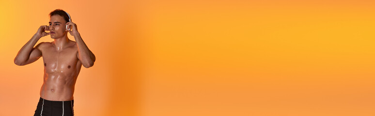 Fototapeta premium young sporty man posing topless while wearing headphones and looking away on vivid backdrop, banner