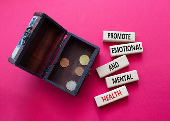 Health symbol. Wooden blocks with words Promote Emotional and Mental Health. Beautiful red background with money box. Health concept. Copy space.