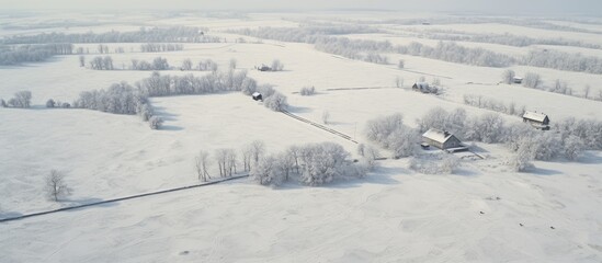 A snow-covered rural field with a house and trees from an aerial perspective