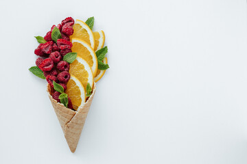 orange slices, raspberries and mint leaves in a waffle cone on a white background