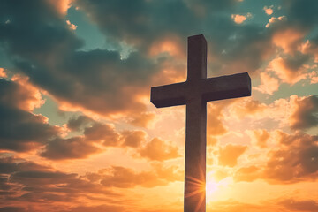 A large cross is standing in front of a cloudy sky. The sky is orange and the sun is shining brightly