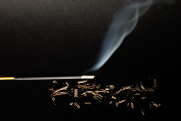 Ashes with an incense stick and its fume on the blurry grey textured background for graphic and web...