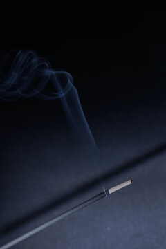 A closeup of incense stick and a knee shaped fume on the black textured background for graphic and web design use