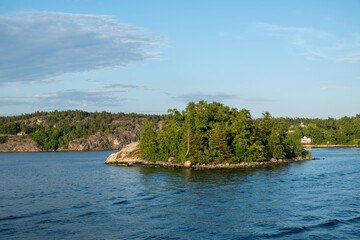 Fototapeta na wymiar Archipelago Stockholm Sweden. Islet with lush nature in Baltic rippled sea. View from cruise boat.