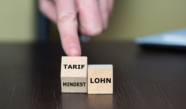 Hand dreht W&uuml;rfel und &auml;ndert den Ausdruck Mindestlohn in Tariflohn.