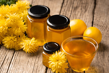 Honey in a jars and in a bowl, honey spoon, lemon, flowers on a wooden background.