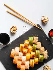 Flat lay of various sushi rolls placed on stone board with chopsticks and soy sauce on gray background