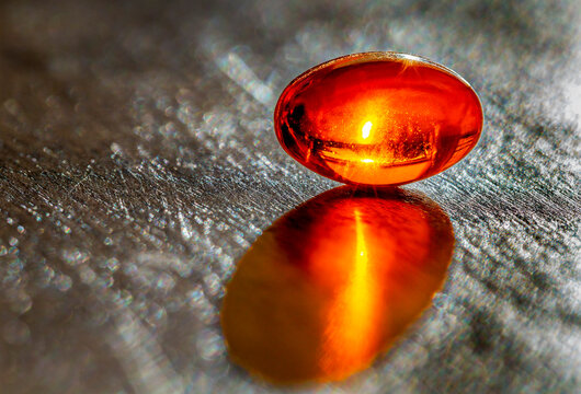 Close up of a glowing gel capsule with a sun glow inside on a grey slate background; Studio Shot