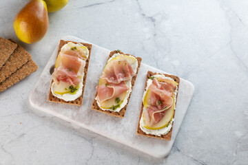 Ideal snack wholewheat crispbread with ricotta cheese, prosciutto, sliced pear and thyme on light...