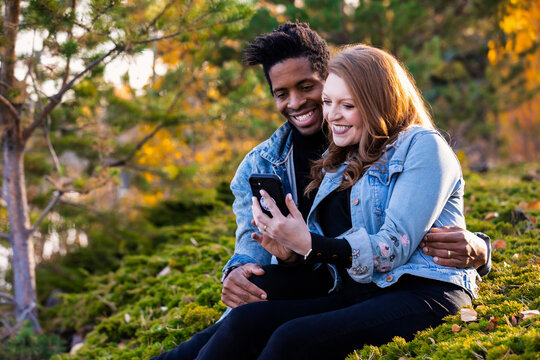 A mixed race couple looking at phone together in a city park in the fall, Edmonton, Alberta, Canada