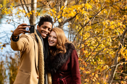 Close-up of a mixed race married couple taking a selfie while spending quality time together during a fall family outing in a city park; Edmonton, Alberta, Canada